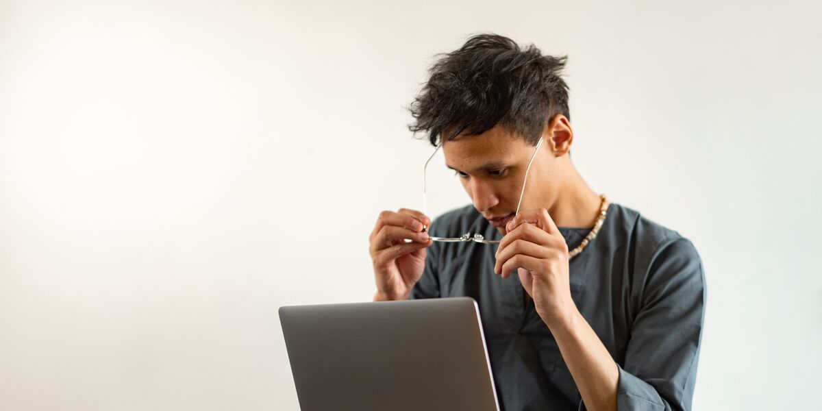 Young man with a laptop on his knees adjusting his glasses