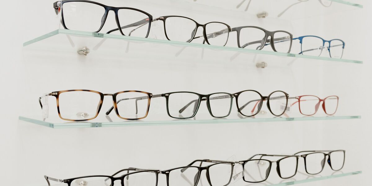 Rows of eyeglass frames in different shapes and colours on glass shelves
