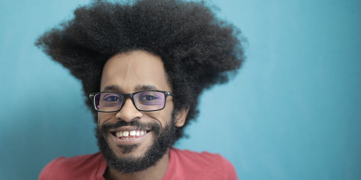 Smiling man with a beard wearing rectangular glasses, facing the camera against a blue wall