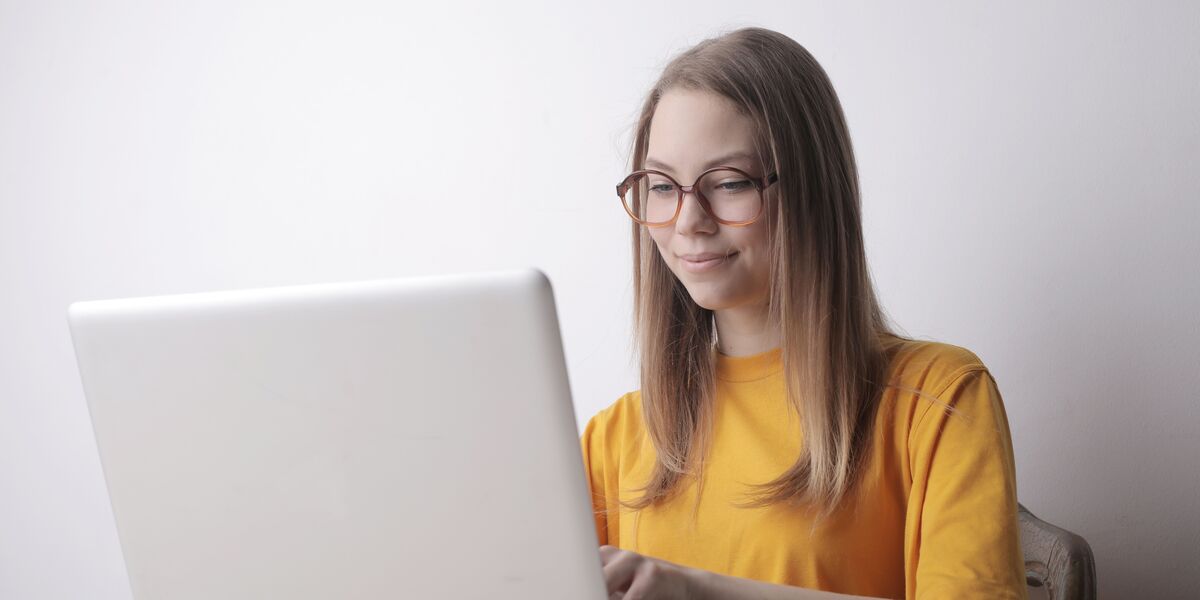 Woman in glasses smiling while typing on a laptop at a table