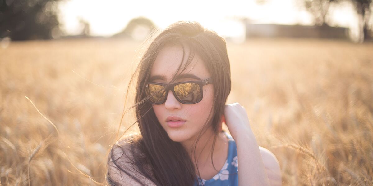 Woman wearing dark tinted glasses sitting in a sunlit field
