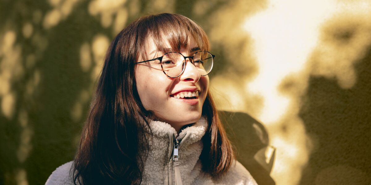Smiling young woman in round metal glasses standing outdoors in warm sunlight